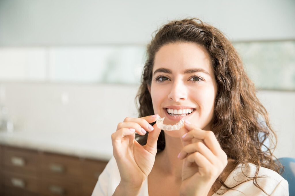 A clear orthodontic aligner tray held between finger and thumb