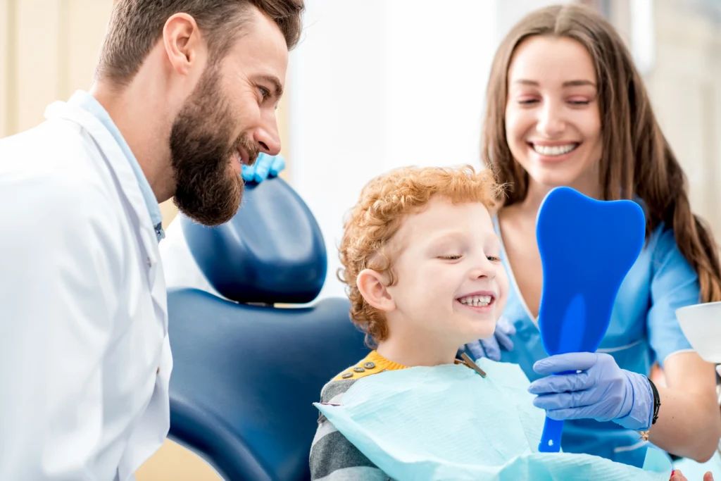 Dentist examines a child's teeth with a dental mirror and explorer while the child smiles.